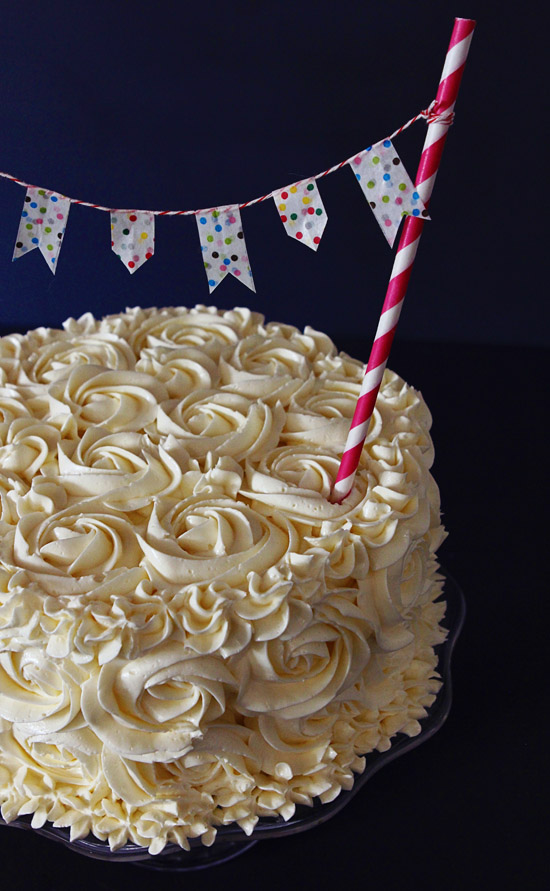 完成后的蛋糕上覆盖着白色的糖霜玫瑰，蛋糕外面伸出一根吸管，上面举着一面横幅。